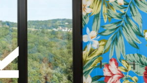 Blick durch ein Fenster der JKU mit Wald, daneben große bunte exotische Blumen auf einer Wand